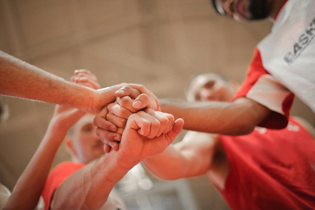 pexels-photo-3755440-3755440 From below of crop multiethnic team of professional basketball players gathering and putting hands together while standing on playground before game
