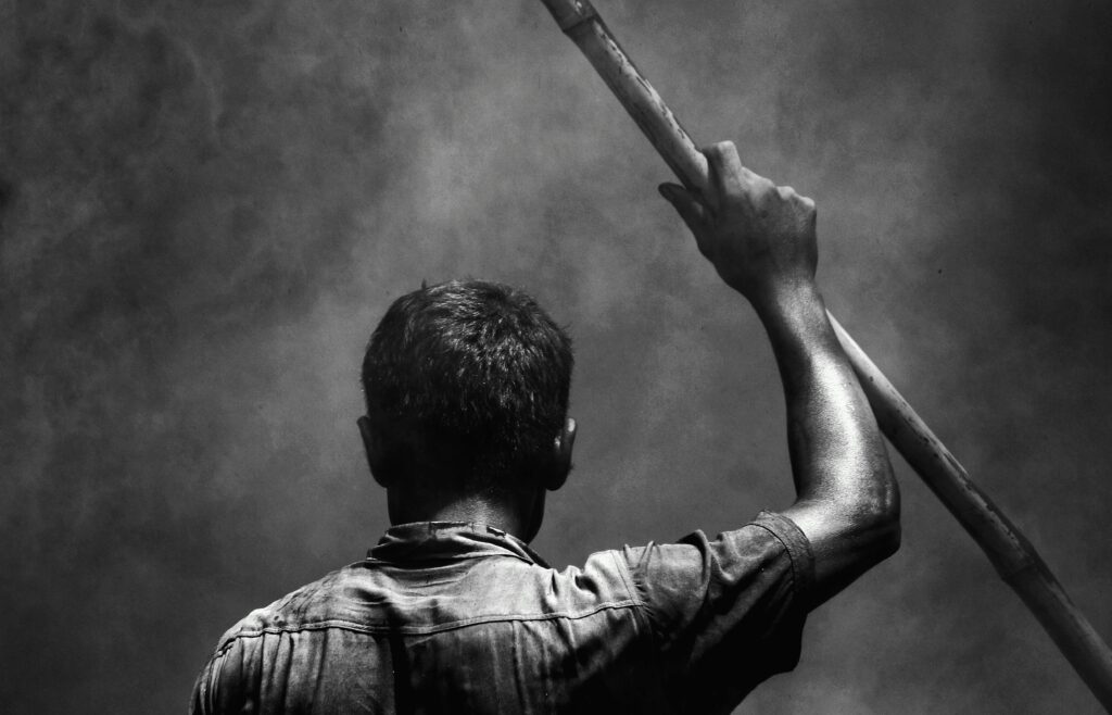 pexels-photo-7573658-7573658 Dramatic black-and-white image of a man from behind, raising a stick into the smoky air.
